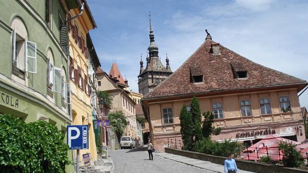 Cobbled street climbing toward Sighișoara Clock Tower, colorful houses