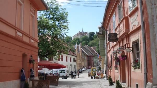 Cobbled street with pastel houses in Sighișoara, citadel visible on the hill
