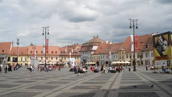 Tourists sitting on Brașov's cobbled square among colorful houses and lampposts