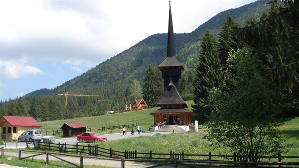 Wooden church with tall spire in mountain valley, tourists walking on grass