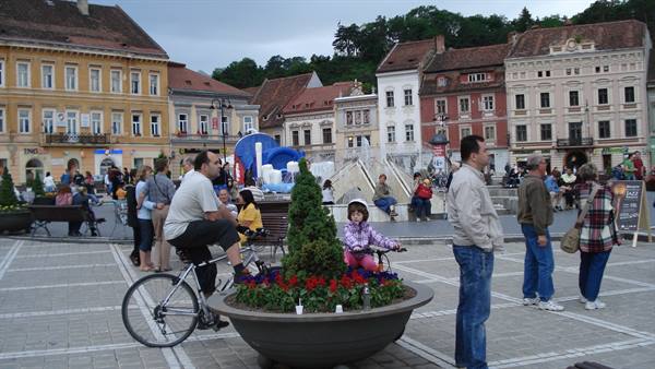 Cyclists and tourists in Brașov's Council Square among colorful baroque buildings
