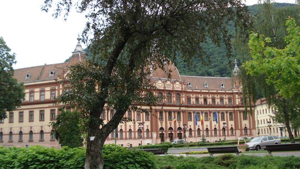 Red and cream domed building behind trees in Brașov
