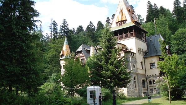 Stone castle with pointed towers among green fir trees, daylight