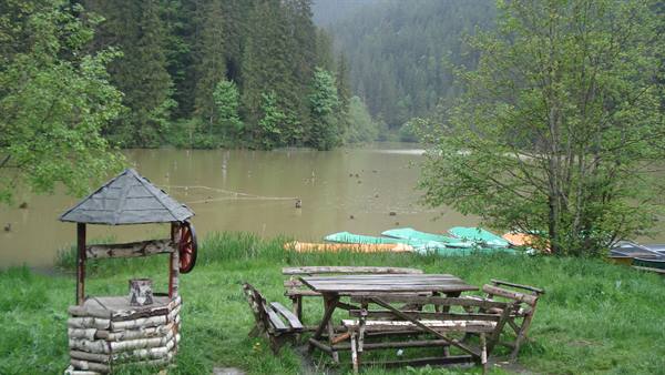 Lake with green canoes and wooden well beside log picnic tables