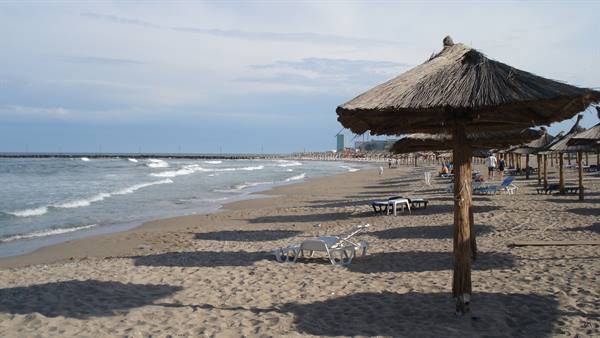 Straw umbrellas on sandy beach with sun loungers and waves under cloudy sky