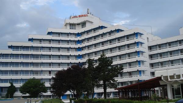 Large 1970s hotel with blue balconies and cloudy sky above the trees