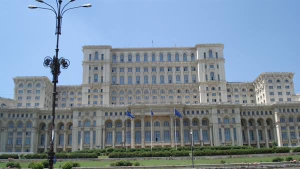 The Palace of Parliament in Bucharest, white stone facade, flags waving under blue sky