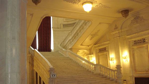 White marble staircase with balustrades, glowing chandeliers and red curtains