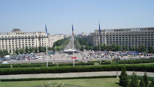 Bucharest, Unirii Boulevard: Romanian flags, parking lots and buildings under blue sky
