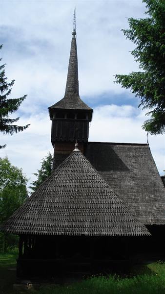 Wooden church with shingled roof and tall steeple among fir trees