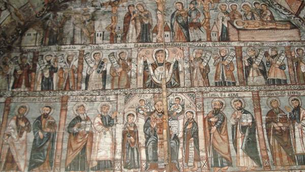Ancient sacred frescoes on a church wall, painted saints in overlapping rows