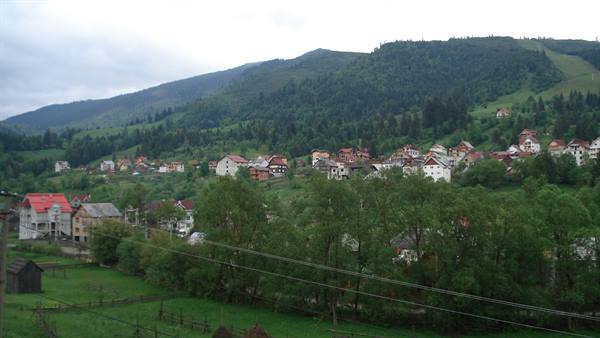 Village of red-roofed houses among forested hills under grey sky