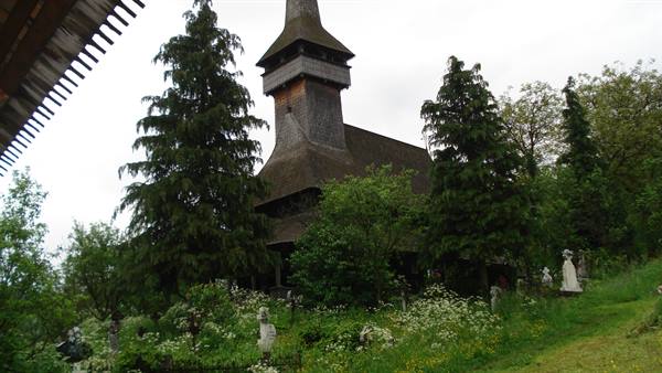 Wooden church with tall shingled steeple among fir trees and white crosses