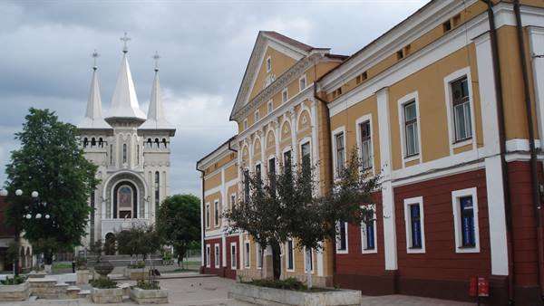 White church with spires beside yellow and red buildings under cloudy sky