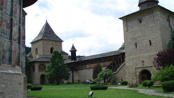 Sucevița Monastery: frescoed wall, stone towers and green courtyard