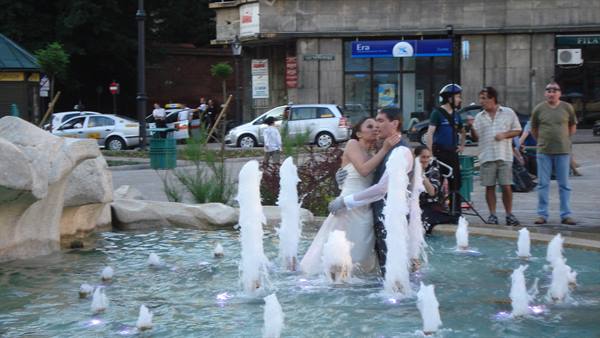 Bride and groom standing inside a city fountain among water jets