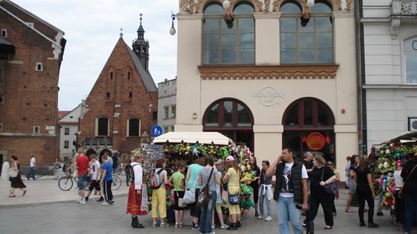 Tourists browsing flower stalls on Krakow's main square, red brick church behind