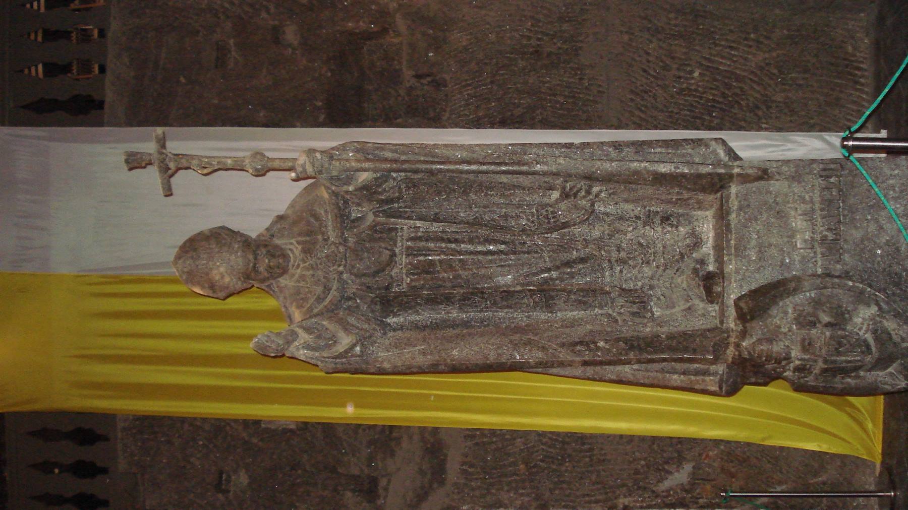 Stone statue of a bishop with pastoral staff, resting behind yellow drapery
