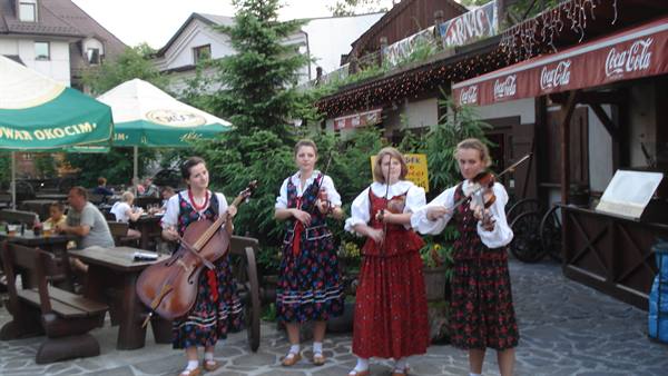 Four musicians in traditional dresses play violins and cello outside a restaurant