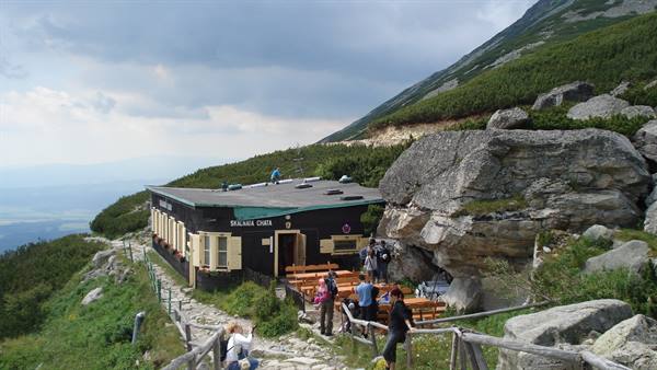 Hikers resting outside Skalnatá Chata mountain hut, granite boulders and cloudy sky