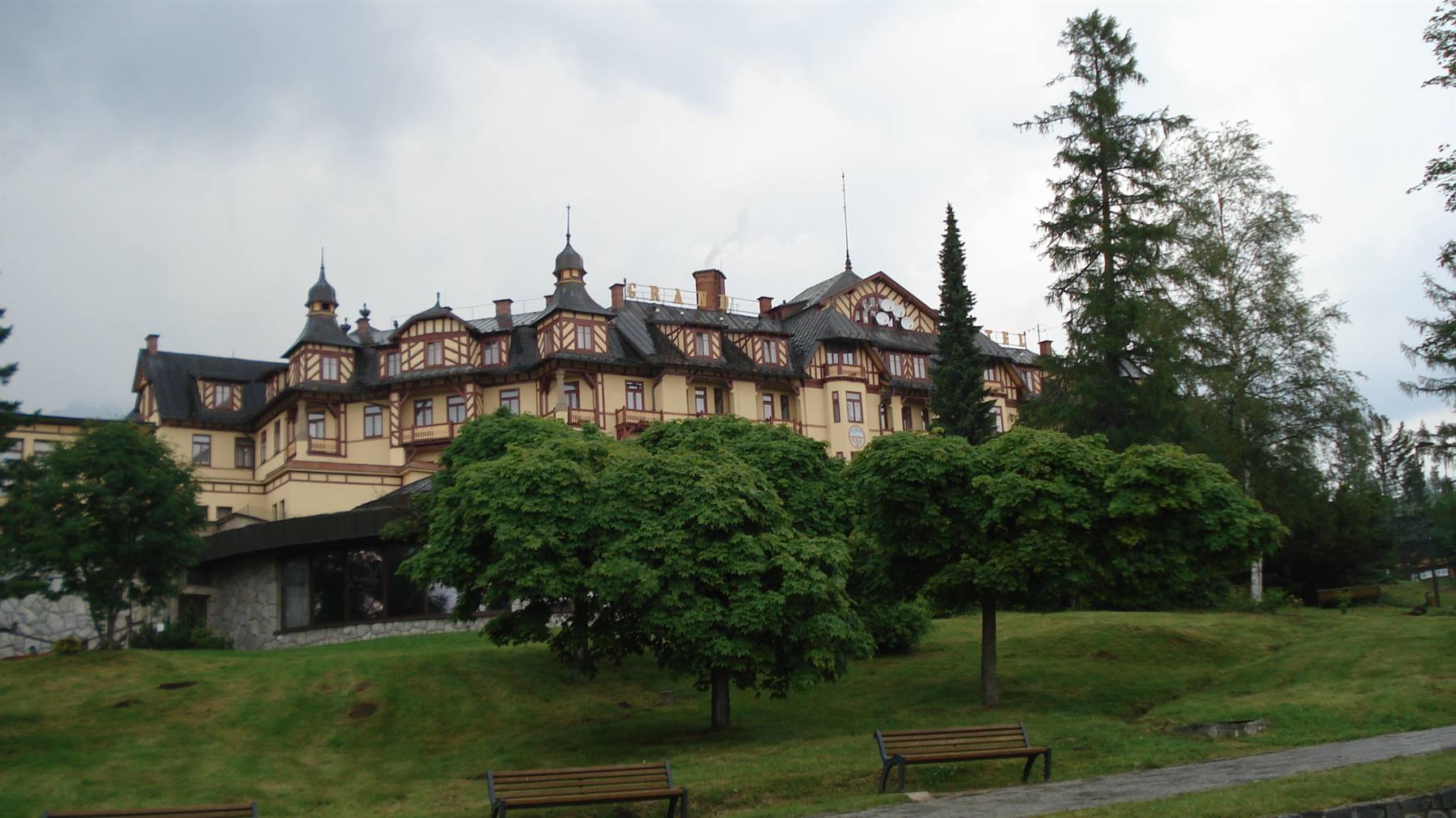 Grand Hotel at Štrbské Pleso, yellow timber facade among firs and benches