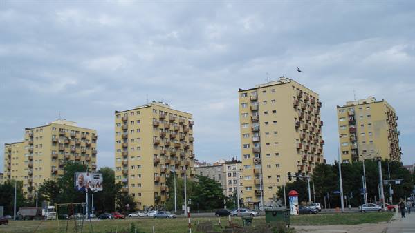 Yellow residential apartment blocks with balconies under cloudy sky, cars on street