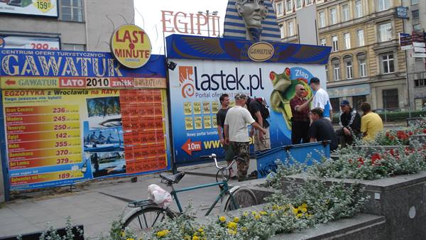 Group in front of travel agency billboards, bicycle parked nearby