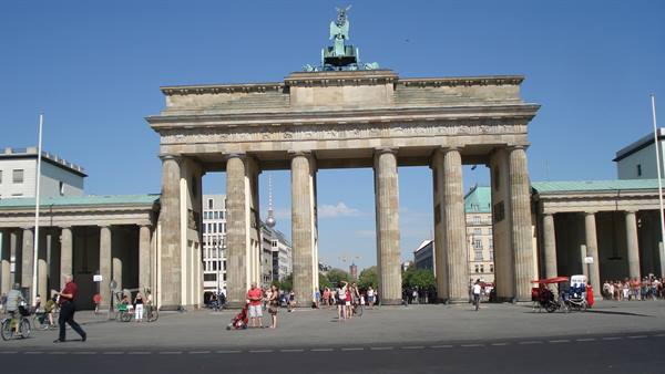 Tourists and cyclists walk in front of the Brandenburg Gate under a blue sky