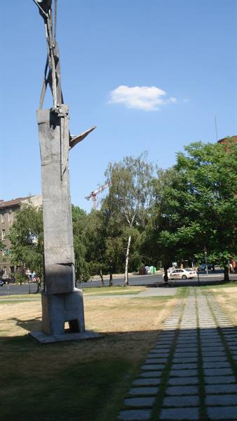 concrete sculpture with metal beams, paved path, trees, blue sky