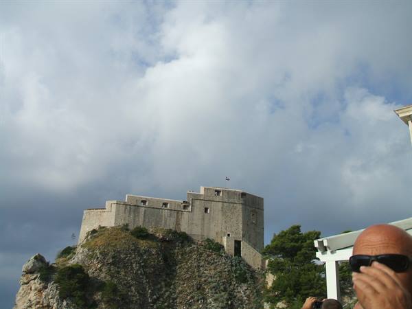Lovrijenac fortress in stone on rocky cliff, cloudy sky, tourists nearby
