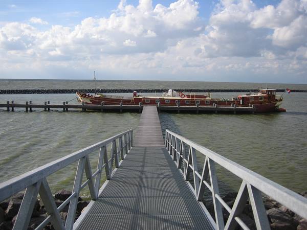Metal footbridge leading to a red moored barge on the IJsselmeer, scattered clouds