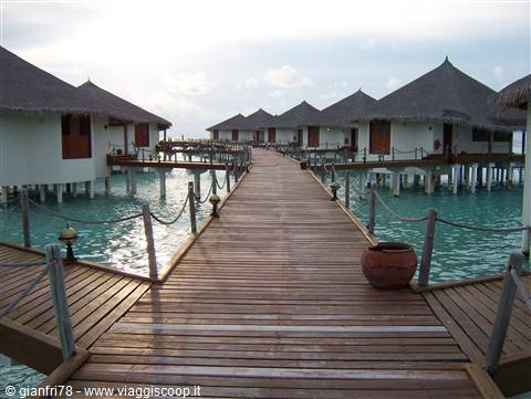 Wooden boardwalk between overwater bungalows above turquoise lagoon water