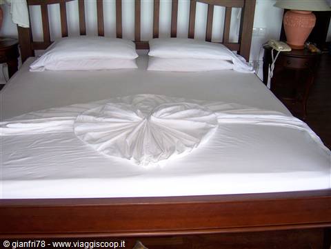 Wooden bed with white sheets and duvet folded into a heart shape