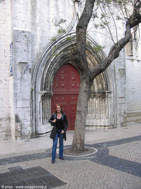 Woman before the red Gothic church portal with tree and cobblestones