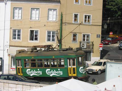 Green tram with Carlsberg advertising turning along a Lisbon street