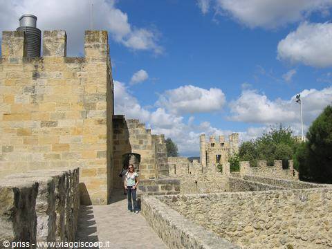 Tourist walking along the battlements of São Jorge Castle, golden stone under blue sky