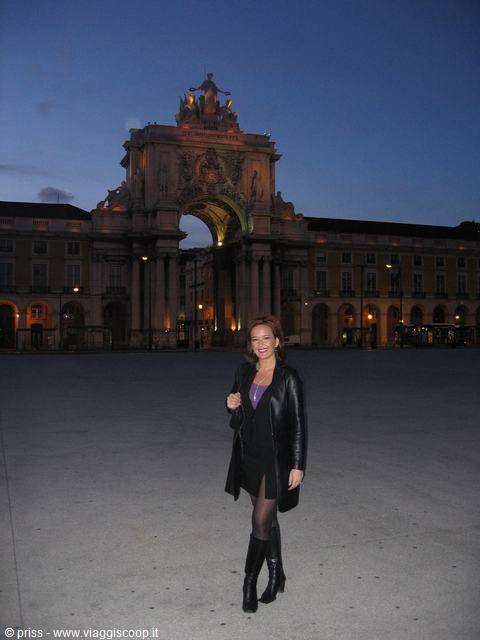 Smiling woman in black coat under the Rua Augusta Arch in Lisbon at dusk