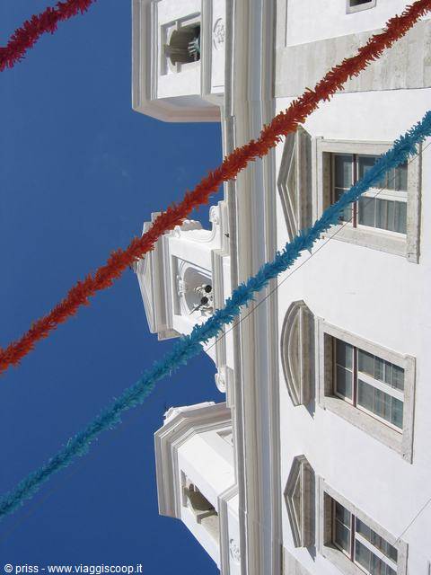 White baroque church facade with red and turquoise garlands against blue sky