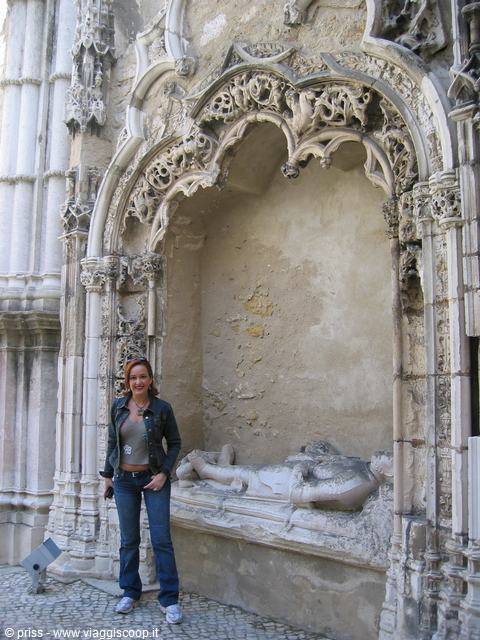 Woman in jeans beside a carved gothic stone niche with a sculpted tomb