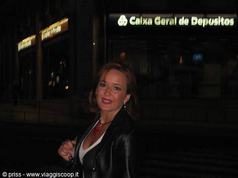 Smiling woman in leather jacket outside Caixa Geral de Depósitos bank at night