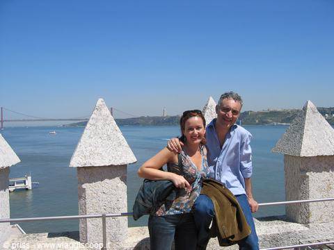 Couple smiling on white battlements of Belém Tower, bridge over Tagus