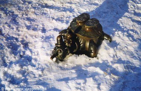 Bronze turtle sculpture half-buried in snow under sunlight