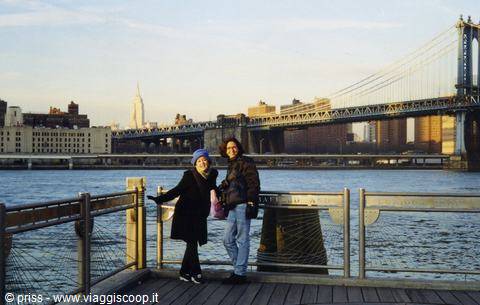 Two tourists on Brooklyn pier, Manhattan Bridge and skyline in background