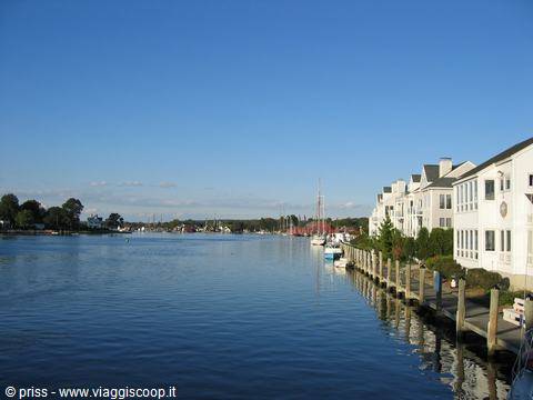 White houses along wooden pier, moored boats, calm water under blue sky