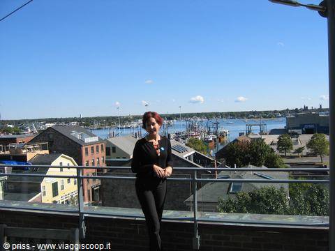 Smiling woman leaning on railing above Gloucester harbor with fishing boats