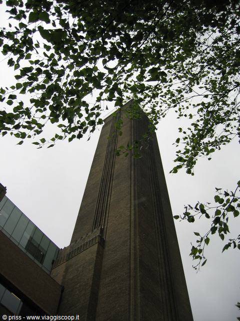 Tate Modern chimney framed by green leaves, grey sky above