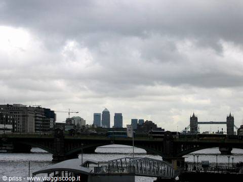 Tower Bridge over the Thames under cloudy sky, with Canary Wharf skyscrapers