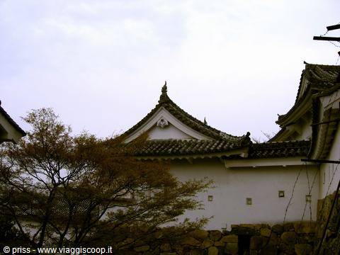 Tetti intonacati bianchi e mura di pietra del castello di Himeji, sotto un cielo grigio