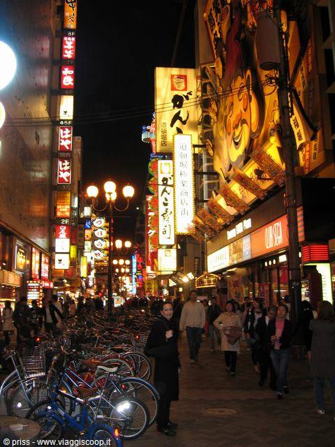 Smiling woman among bicycles and glowing neon signs on a busy Osaka street