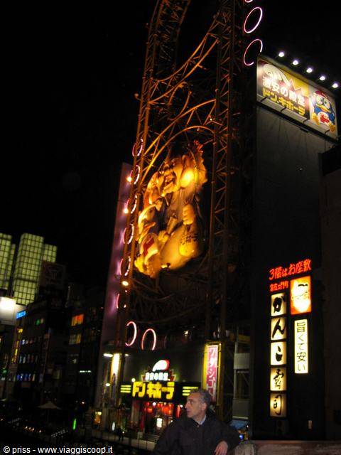Man stands before Dotonbori's glowing neon signs and ferris wheel at night
